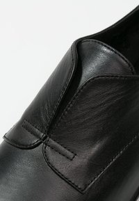 Czarny skórzany but o gładkiej fakturze, z zaokrąglonym noskiem i wsuwanym fasonem z asymetrycznym detalem klapki z przodu.