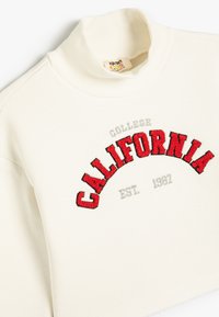 Crèmekleurige sweatshirt met een hoge ribbelkraag, met rode geborduurde tekst "CALIFORNIA" en grijze accenten. Zacht katoen materiaal.