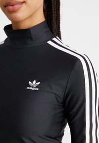 Zwart sporttop met hoge kraag, voorzien van witte strepen op de mouwen en een klein wit Adidas-logo op de borst. Soepele textuur.
