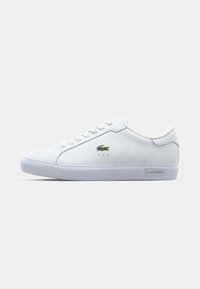Biały skórzany sneaker z zielonym logo Lacoste, gładką powierzchnią, okrągłym noskiem, płaską białą gumową podeszwą i sześcioma dziurkami na sznurowadła.