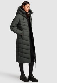 Langer, wattierter Mantel in Dunkelgrün mit großer Kapuze, Reißverschluss, Seitentaschen und vertikalen Steppnähten. Strukturierter Stoff mit glatter Oberfläche.