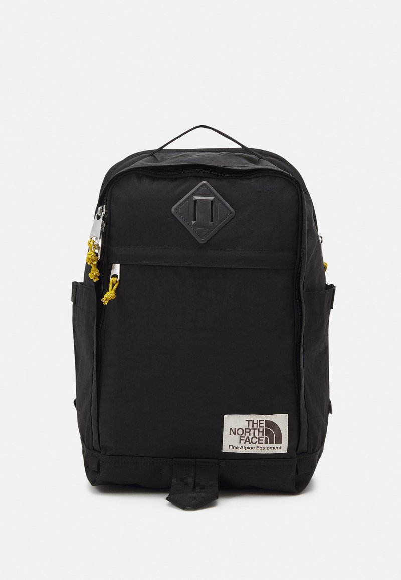 Sac à dos noir The North Face avec poche avant zippée, tirettes de fermeture éclair jaunes, poignée supérieure, poches latérales et écusson logo en bas à droite.