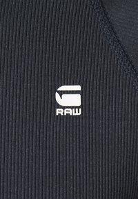 Marinblå ribbad tyg med en framträdande vit "RAW"-logotyp. Har en strukturerad yta och en rundad halsringning.