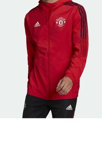 Chaqueta roja con cremallera completa, con franjas negras en las mangas, logo del Manchester United y material ligero y resistente al agua.