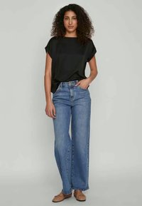 Must have lühikeste varrukatega must topp, lõdva lõikega. Heledat sinist laiade sääruitidega teksad, kõrge vöökohaga. Beezid slip-on kingad, siledat tekstuuri. Minimalistlik stiil.