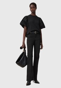 Top nero con maniche a sbuffo abbinato a pantaloni neri a zampa. Gli accessori includono una borsa nera e tacchi a punta. Tessuto liscio, design aderente.