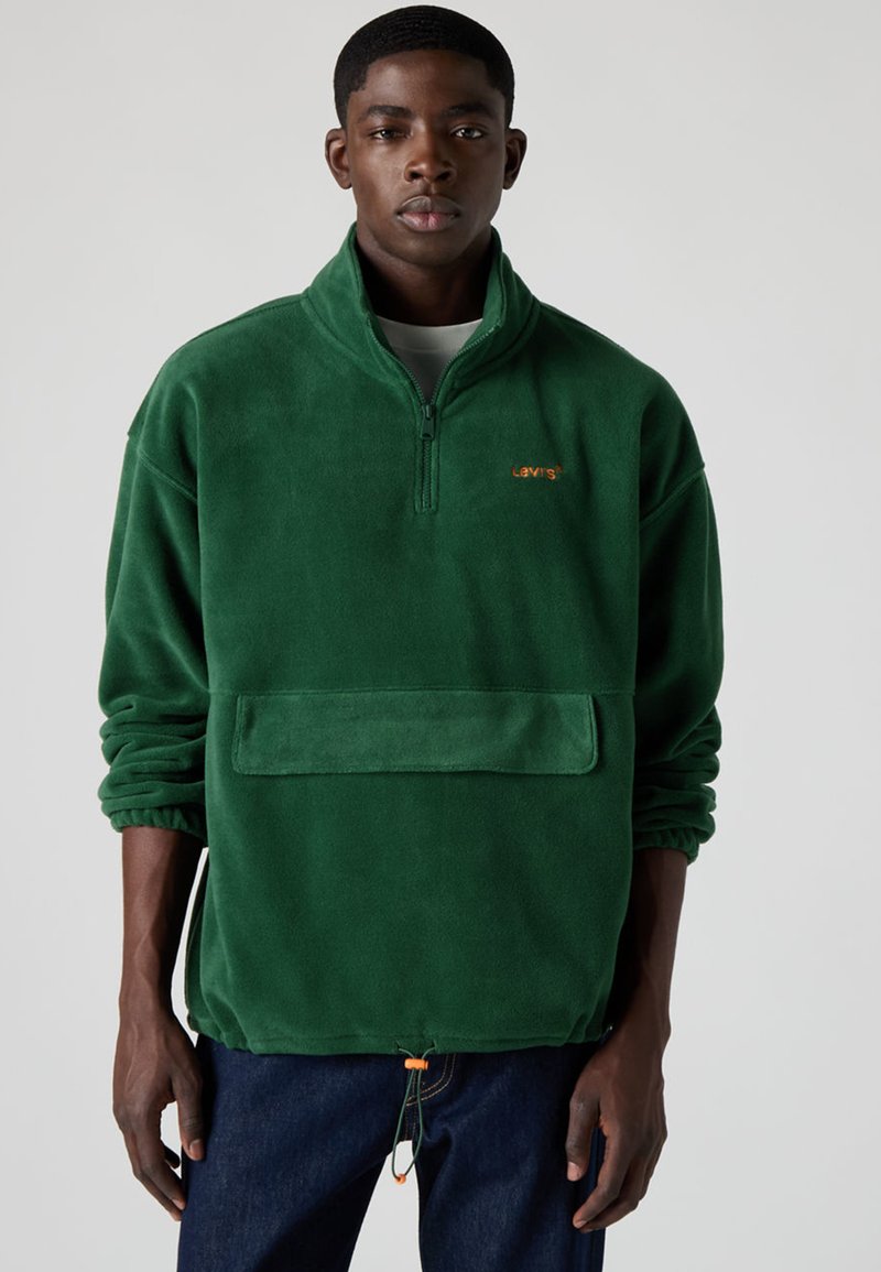 Grön fleecetröja med halvlång dragkedja i kragen, framficka och elastiska muddar. Har en orange Levi's-logga och dragsko i fållen.