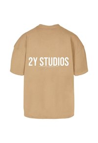 Camiseta marrón de gran tamaño hecha de algodón, con un logo impreso en blanco "2Y STUDIOS" en la parte de atrás. Mangas cortas y un corte relajado.