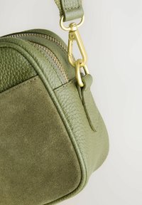 Olijfgroen leren en suède tas met een gestructureerde afwerking, dubbele rits en goudkleurige hardware. Compacte vorm met een stevige schouderband.