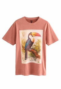 Rust-colored T-shirt with a large graphic of a toucan perched on a branch, with "GUINNESS" text and harp logo above.