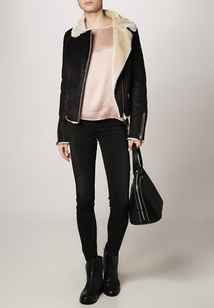 Zwarte shearling jas met crème voering, gedragen over een blush satijnen top. Gecombineerd met zwarte skinny jeans en enkellaarsjes. Zwarte tas met hardware accenten.
