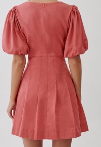 Růžový šaty s vypouklými rukávy, skládáním sukně a zipem na zadní straně. Vlastnosti zahrnují strukturovaný korzet s kulatým výstřihem.