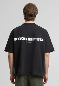 Zwart katoenen T-shirt met korte mouwen, met op de achterkant vetgedrukte witte tekst "PROHIBITED" en "10119, BERLIN". Klassieke relaxte pasvorm.