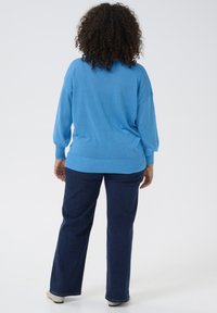 Blauwe gebreide trui met een ontspannen pasvorm, lange mouwen en ribbelrand; gecombineerd met donkerblauwe rechte spijkerbroek. Soepele textuur, casual stijl.