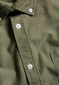 Olivgrön skjorta med knäppkrage, vita plastknappar, texturerad tyg och en bröstficka.