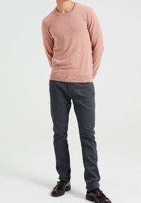 Ljust rosa stickad tröja med rund halsringning, i kombination med mörkgrå slim-fit byxor och svarta skor, som skapar en kontrasterande färgpalett.