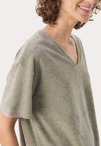 Siva-zelen v-neck majica iz mehkega materiala, z kratkimi rokavi in sproščenim krojem, z minimalnimi šivi.