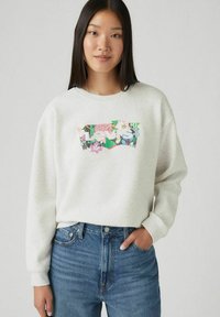Sweatshirt gris avec un col rond, orné d'un motif floral en rose, vert et bleu. Assorti à un jean taille haute bleu.