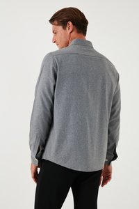 Grijs overhemd met lange mouwen, subtiele textuur en zijsplitten. Tailored fit en witte knoopdetails op de manchetten. Zwarte broek zichtbaar.