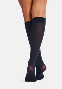 Knæhøje sokker i mørk navy, semi-transparent materiale med en bølget kantdesign, glat tekstur og forstærket hæl.