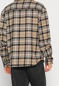 Brun och svart rutigt flanellskjorta med avslappnad passform, knäppte ärmar och rundad nederkant. Har en mjuk, strukturerad tyg.