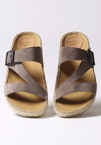 Sandali in suede marrone con design incrociato, fibbia nera e suola intrecciata beige. Fodera interna morbida e punta arrotondata.