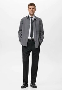 Camisa de cuadros en blanco y negro sobre una camisa blanca, combinada con pantalones y zapatos negros, presentando una corbata y un cinturón negros simples.
