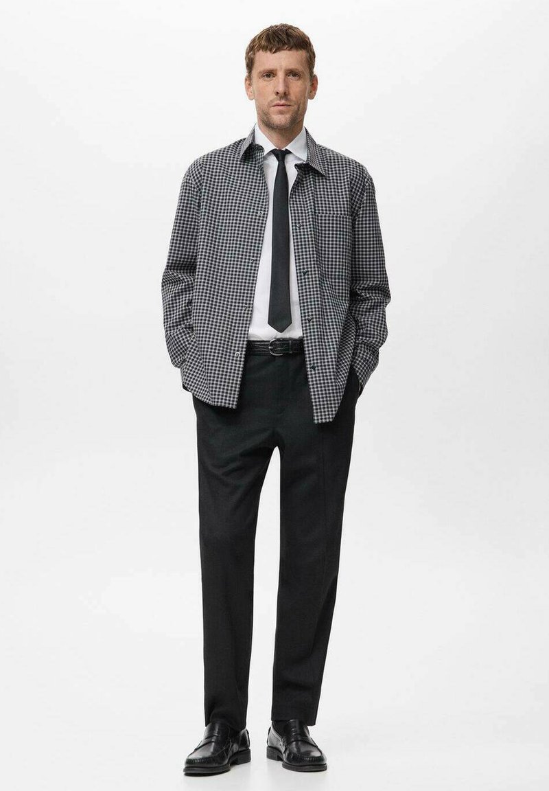 Black and white checkered shirt over a white dress shirt, paired with black trousers and shoes, featuring a simple black tie and belt.