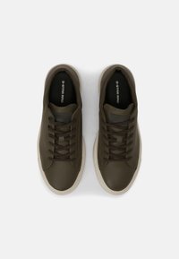 Ciemnozielone sneakersy z gładkiego, błyszczącego materiału, o okrągłym czubku, z brązowymi sznurówkami, teksturowanym bocznym panelem i jasną podeszwą.