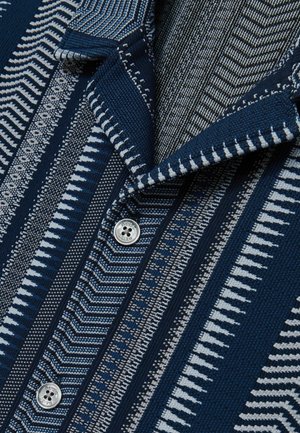 Navy and gray patterned shirt featuring various textures, with a collared neckline and a button closure. Distinct diagonal and striped designs.