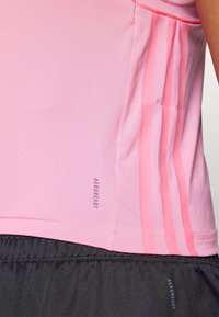 Jasnoróżowa koszulka sportowa z gładką fakturą, krótkimi rękawami i trzema różowymi pionowymi paskami po boku, oznaczona napisem "AEROREADY."