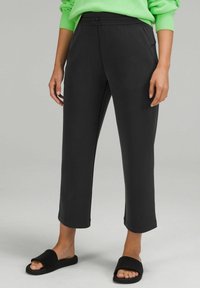 Person som bär avklippta svarta byxor med sidofickor, matchat med svarta halkskor och en ljusgrön långärmad tröja.