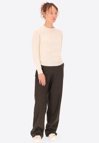 Maglione aderente beige chiaro con maniche lunghe, abbinato a pantaloni a quadri marroni e sneakers bianche; tessuto morbido e design semplice.