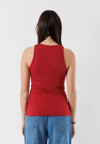 Top rosso senza maniche in un tessuto liscio e elasticizzato, design aderente, con scollatura rotonda e schiena senza cuciture, abbinato a jeans blu a vita alta.