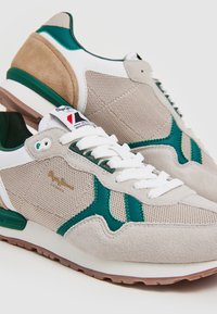 Sneakers atletici beige e verdi con materiali in rete e suede, dotati di lacci bianchi, colletto imbottito e suola in gomma testurizzata.