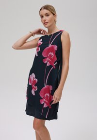 Ärmelloses Kleid aus marineblauem Stoff mit großen rosa Orchideenmustern, lockerer Schnitt und seitlichen Schlitzen für Bewegungsfreiheit; glatte Textur.