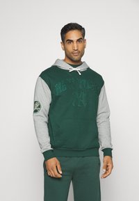 Sudadera con capucha de cuerpo verde oscuro y mangas grises, con "NEW YORK" bordado en el frente y un parche de logo en la manga.