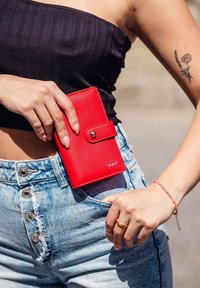 Red leather wallet with a snap closure, placed in the pocket of light blue denim shorts featuring distressed detailing and metallic buttons.