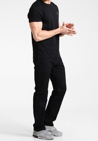 Black short-sleeve t-shirt with crew neck, paired with black jeans. Gray athletic shoes complete the outfit, showcasing a casual appearance.