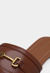 Mocassin marron en cuir à enfiler avec boucle métallique dorée et coutures contrastantes sur la semelle.