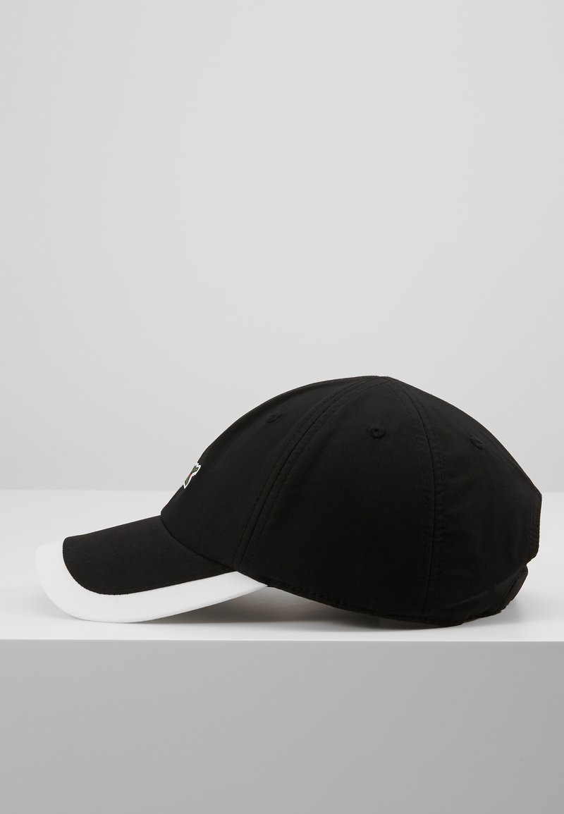 Gorra de béisbol negra con visera blanca, hecha de tela. Presenta detalles de costura y orificios de ventilación en los paneles superiores para transpirabilidad.