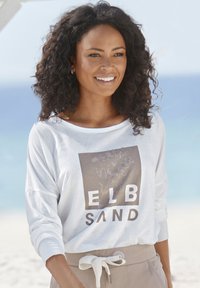Lightweight white long-sleeve shirt with a graphic print reading "ELB SAND," paired with tan pants featuring a drawstring waist and relaxed fit.