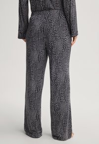 Wijdvallende broek in een zwart en grijs krokodillenpatroon. Gemaakt van een soepele stof met een comfortabele pasvorm en een elastische tailleband.