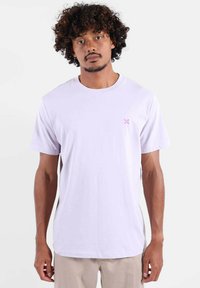 T-shirt manches courtes lavande clair en coton doux. Présente un petit logo rose sur le côté gauche de la poitrine. Col rond, coupe décontractée.
