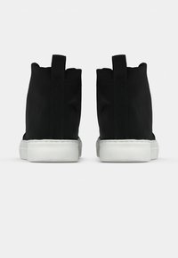 Sorte høyre mosjonsko laget av kanvas med hvit gummisåle, med bakre trekkbelte og et glatt, minimalistisk design.