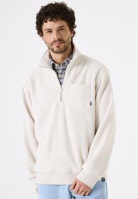 Fleece pullover in crème kleur, voorzien van een half-rits, een voorzak en geribbelde manchetten. Zachte textuur met een relaxte pasvorm.
