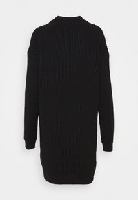 Pull en tricot noir avec une texture côtelée, col haut et manches longues. Le dos a un ourlet légèrement plus long.
