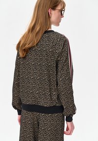 Zwarte bomberjack met luipaardprint, geribbelde manchetten en tailleband. Heeft rood-witte strepen op de mouwen. Zachte stoftextuur.