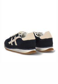 Zapatillas deportivas azul marino con una parte superior de ante y malla, cordones en color blanco roto, acentos en crema y una suela de goma texturizada. Se muestra la vista trasera.