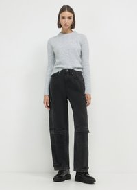 Grauer Strickpullover mit Rundhalsausschnitt, kombiniert mit schwarzen Cargo-Hosen mit mehreren Taschen und lockerer Passform. Schwarze Schnürschuhe.